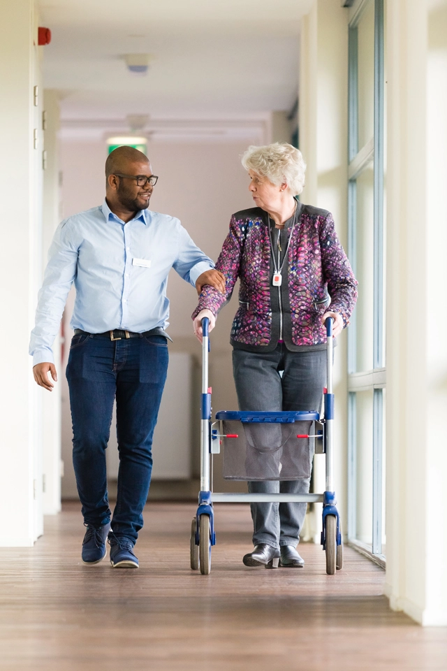 zormedewerker ondersteunt oudere dame met rollator